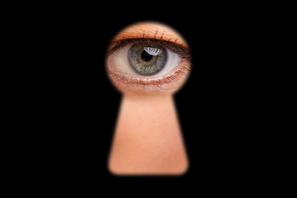 An image of an eye peeping through the keyhole of a door. 